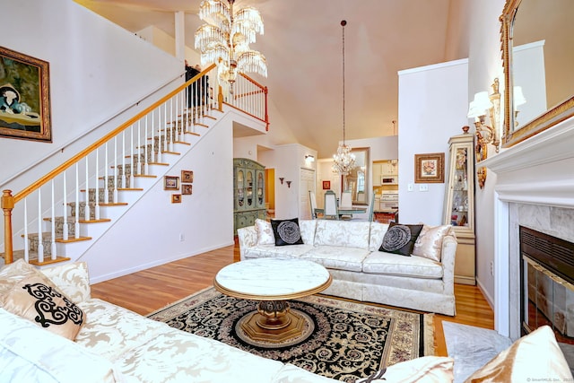 living room with a premium fireplace, wood finished floors, a towering ceiling, stairs, and an inviting chandelier