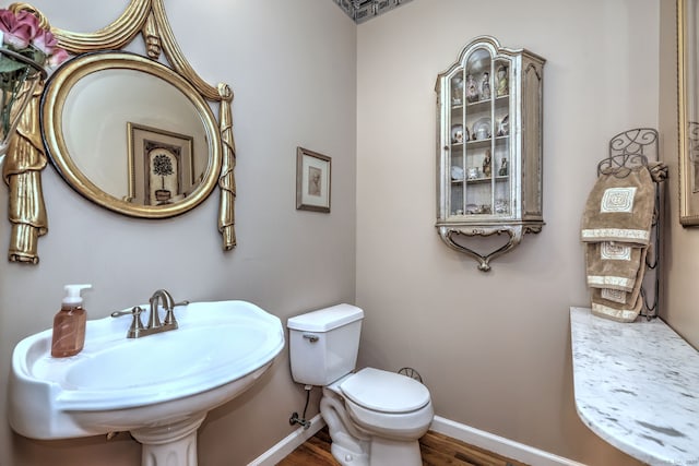 bathroom featuring toilet, a sink, baseboards, and wood finished floors