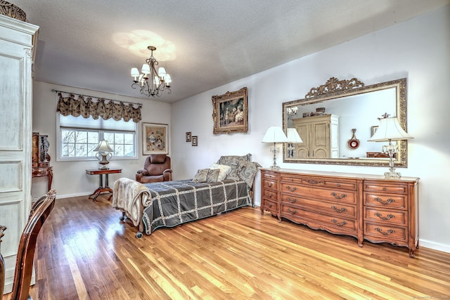 bedroom with light wood-type flooring, a textured ceiling, baseboards, and a notable chandelier