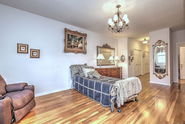 bedroom featuring a textured ceiling, a chandelier, wood finished floors, and baseboards