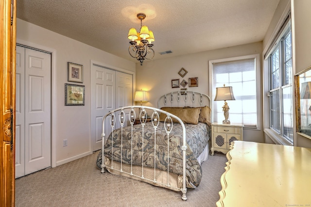 carpeted bedroom featuring an inviting chandelier, baseboards, visible vents, and a textured ceiling