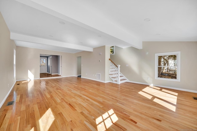 unfurnished living room featuring visible vents, baseboards, stairs, light wood finished floors, and beamed ceiling