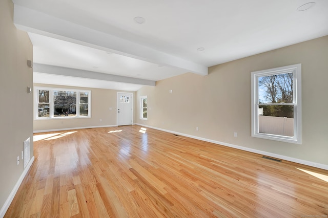 unfurnished living room with light wood-style flooring, visible vents, a wealth of natural light, and beamed ceiling