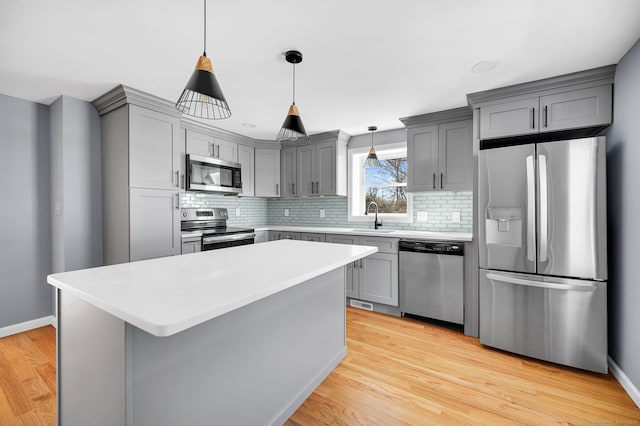kitchen featuring gray cabinets, light countertops, appliances with stainless steel finishes, light wood-style floors, and a sink