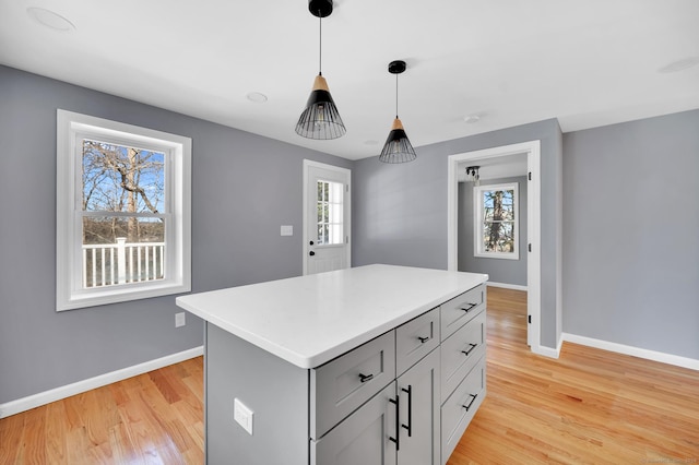 kitchen with a kitchen island, baseboards, hanging light fixtures, light countertops, and light wood finished floors