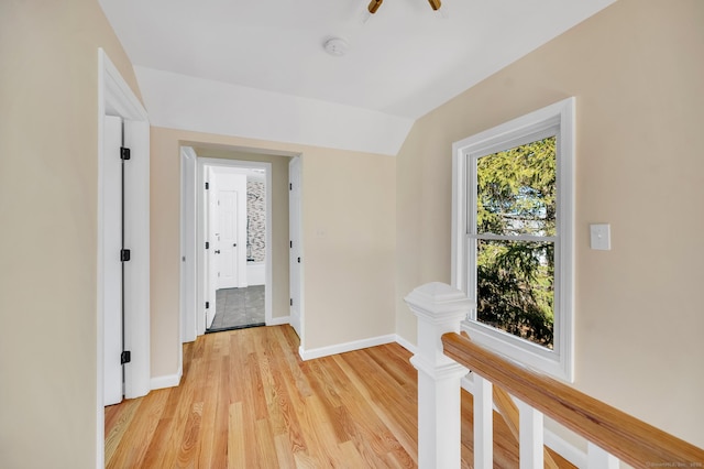 hall featuring lofted ceiling, baseboards, and light wood finished floors