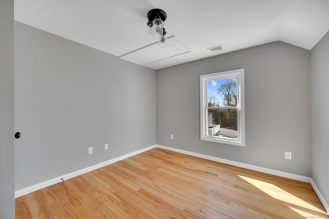 unfurnished room featuring attic access, baseboards, visible vents, wood finished floors, and vaulted ceiling