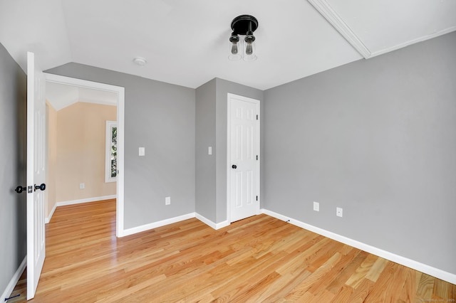 unfurnished bedroom featuring lofted ceiling, a closet, light wood-style floors, attic access, and baseboards