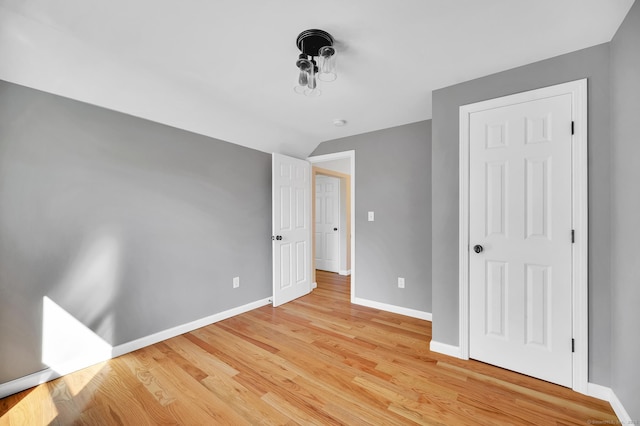 unfurnished bedroom with baseboards, vaulted ceiling, and light wood-style floors