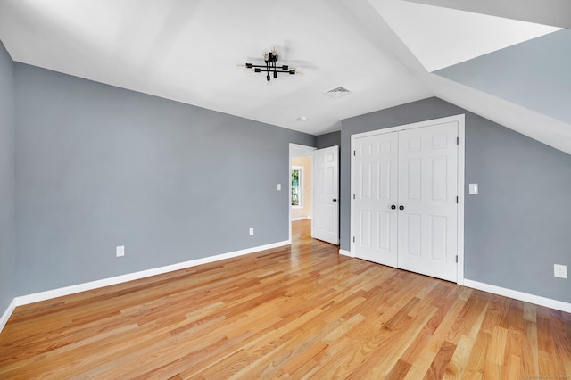 unfurnished bedroom featuring baseboards, visible vents, vaulted ceiling, light wood-style floors, and a closet