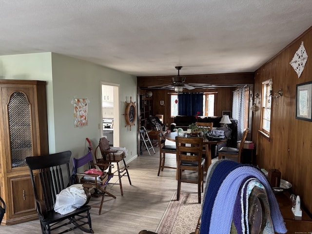 dining room with a ceiling fan, wooden walls, light wood finished floors, and a textured ceiling