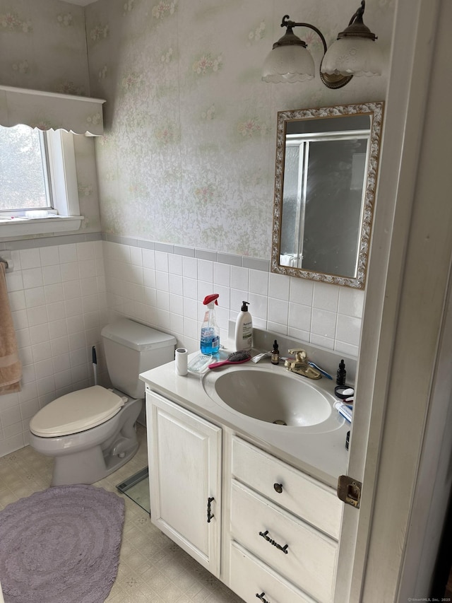 full bath with toilet, tile walls, vanity, a stall shower, and wallpapered walls