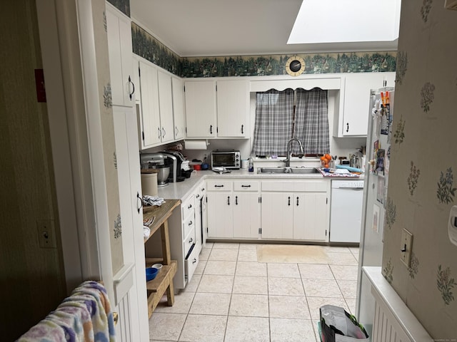 kitchen featuring a skylight, light countertops, light tile patterned flooring, a sink, and dishwasher