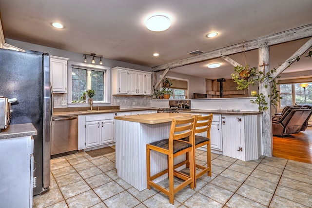 kitchen featuring stainless steel appliances, a kitchen island, a sink, white cabinets, and decorative backsplash