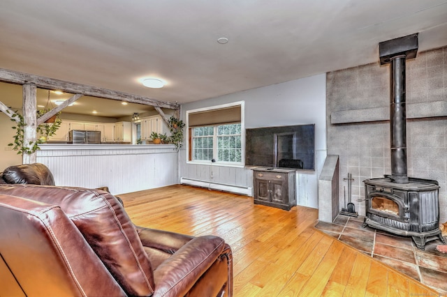 living room with a baseboard radiator, a wood stove, and hardwood / wood-style flooring