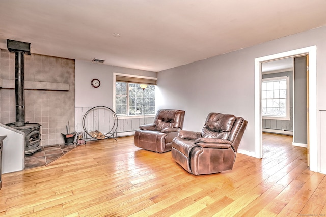 sitting room featuring a wood stove, visible vents, a baseboard heating unit, and hardwood / wood-style floors