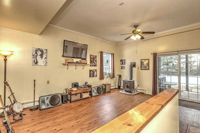 interior space with crown molding, a baseboard radiator, a wood stove, ceiling fan, and wood finished floors