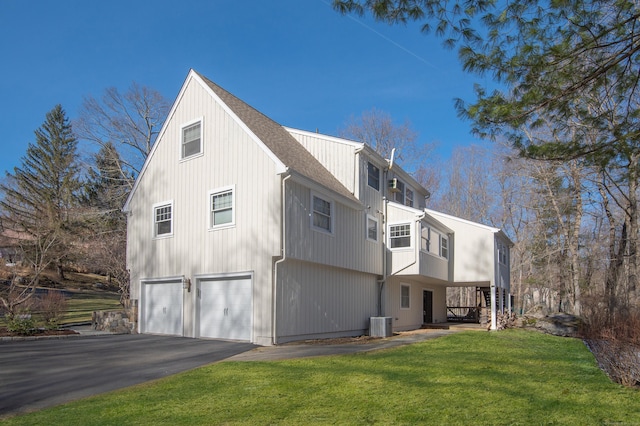 view of side of property with a yard, a shingled roof, an attached garage, cooling unit, and driveway