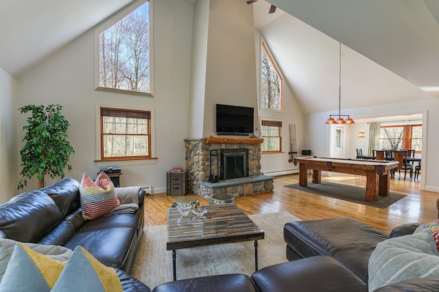 living room featuring high vaulted ceiling, a stone fireplace, a baseboard heating unit, pool table, and light wood-type flooring