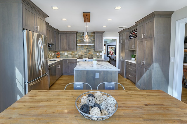 kitchen featuring a sink, dark brown cabinets, appliances with stainless steel finishes, a center island, and wall chimney exhaust hood