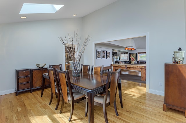 dining area with lofted ceiling with skylight, recessed lighting, light wood-style flooring, and baseboards