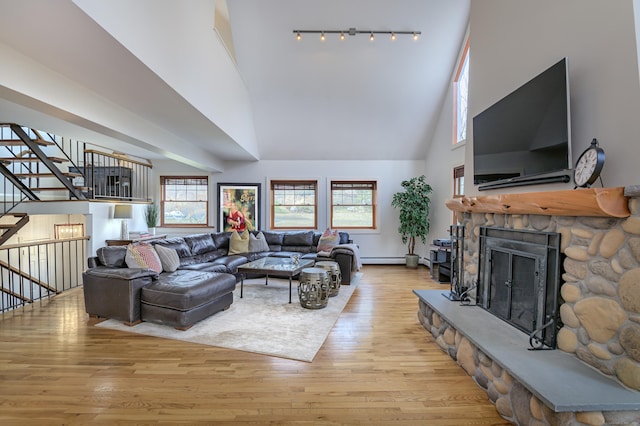 living room featuring a towering ceiling, light wood finished floors, rail lighting, and a stone fireplace