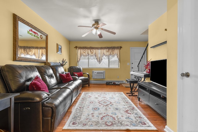 living area with baseboard heating, a wall mounted air conditioner, ceiling fan, and wood finished floors