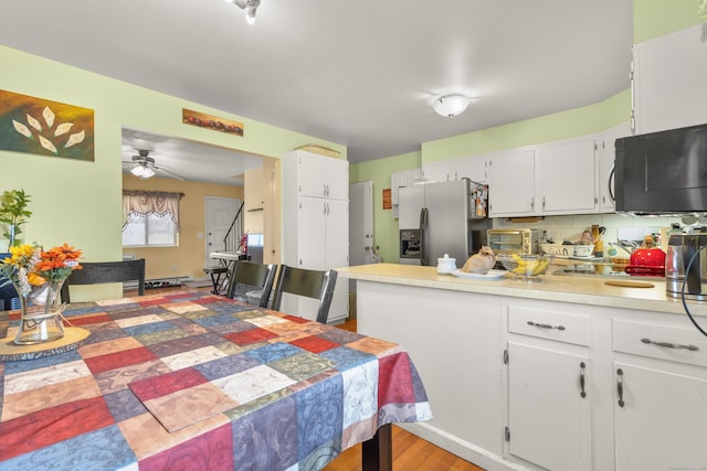 kitchen featuring black microwave, light countertops, a peninsula, stainless steel refrigerator with ice dispenser, and white cabinets