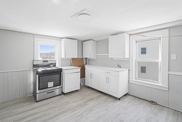 kitchen with a wainscoted wall, stainless steel gas range oven, and white cabinets