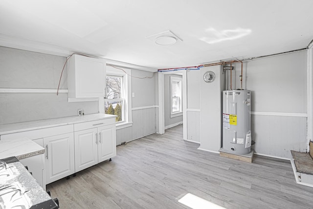 interior space featuring light wood-style flooring, wainscoting, electric water heater, and white cabinets