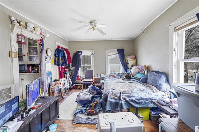 bedroom with ceiling fan, multiple windows, crown molding, and wood finished floors