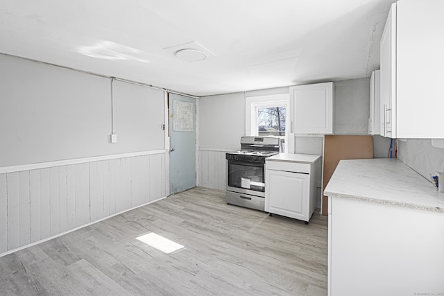 kitchen featuring light wood finished floors, wainscoting, range with gas cooktop, and white cabinets