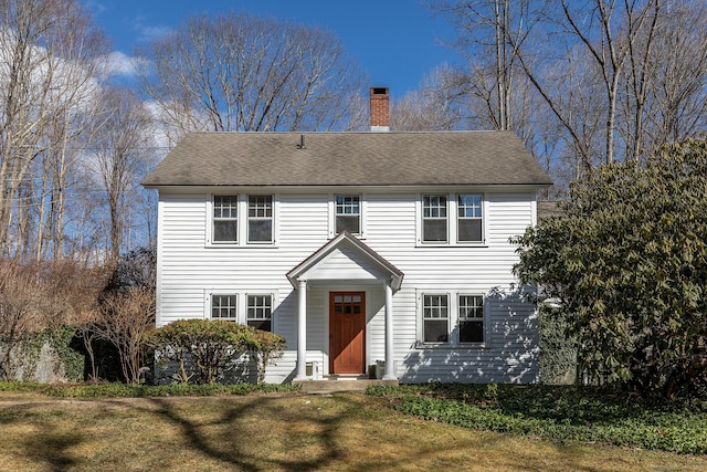 colonial house with roof with shingles, a chimney, and a front yard