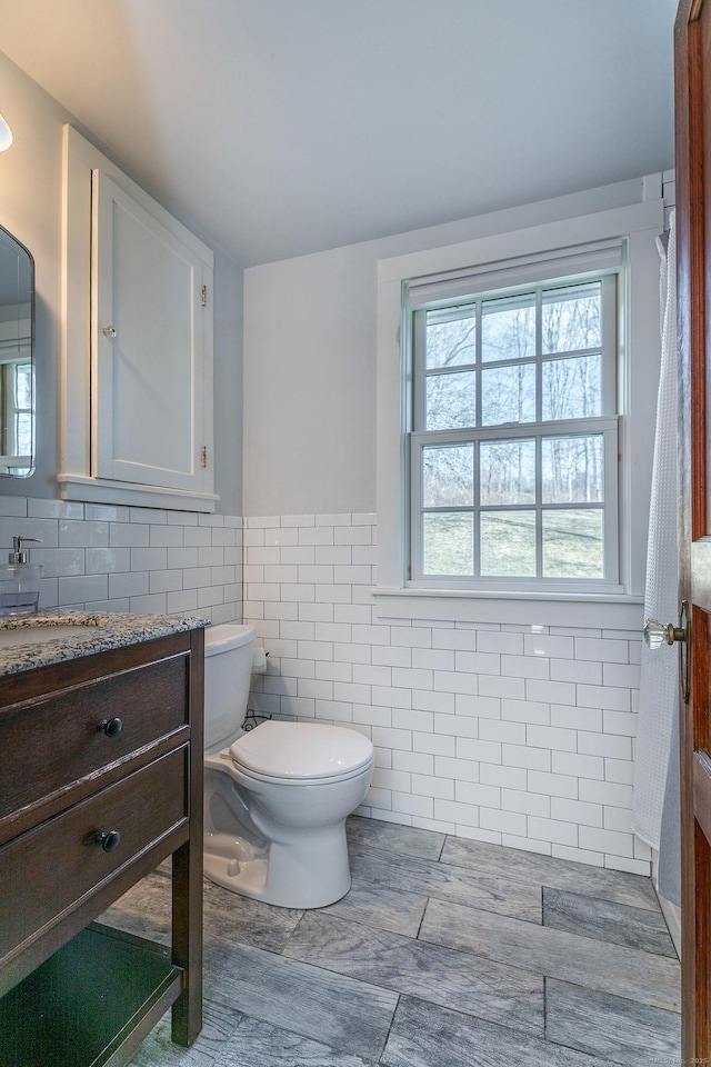 bathroom featuring toilet, tile walls, a wainscoted wall, and vanity