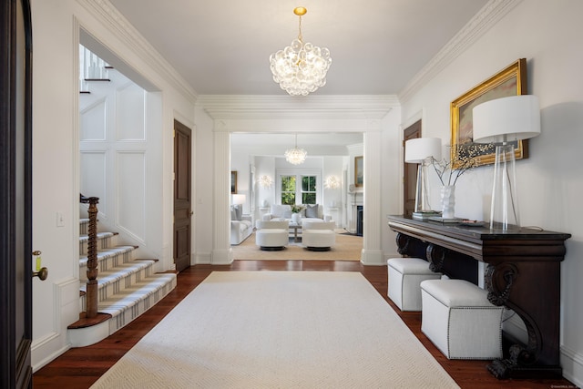 foyer entrance featuring dark wood-style floors, an inviting chandelier, stairs, crown molding, and a fireplace