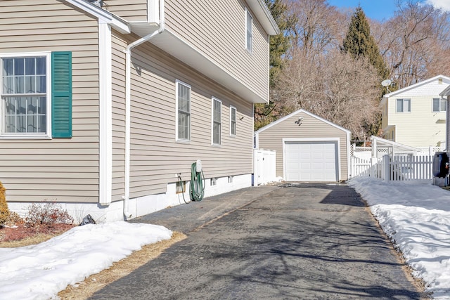 view of snowy exterior featuring aphalt driveway, an outdoor structure, fence, and a detached garage