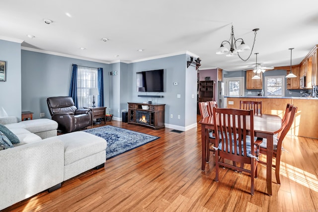 living area featuring crown molding, a lit fireplace, a healthy amount of sunlight, and light wood-style floors