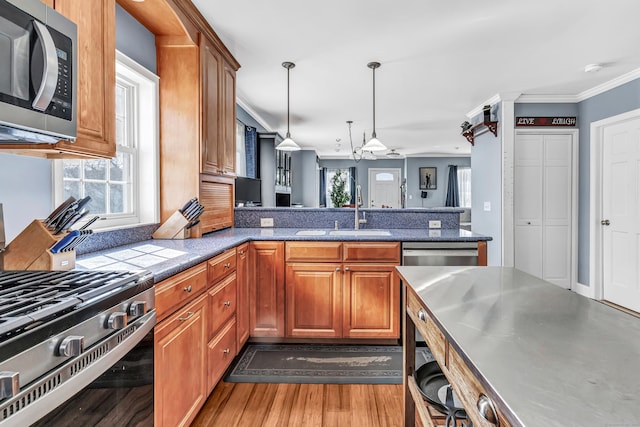 kitchen with crown molding, appliances with stainless steel finishes, brown cabinetry, a sink, and a peninsula