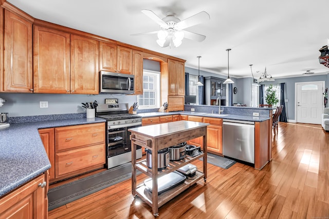 kitchen featuring stainless steel appliances, a sink, a peninsula, and light wood finished floors