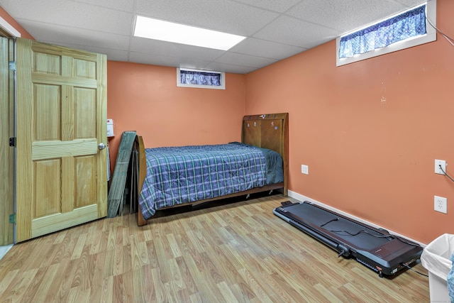 bedroom featuring a drop ceiling, baseboards, and wood finished floors