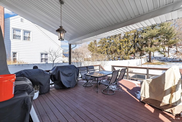 snow covered deck with outdoor dining area, a fenced backyard, and a grill