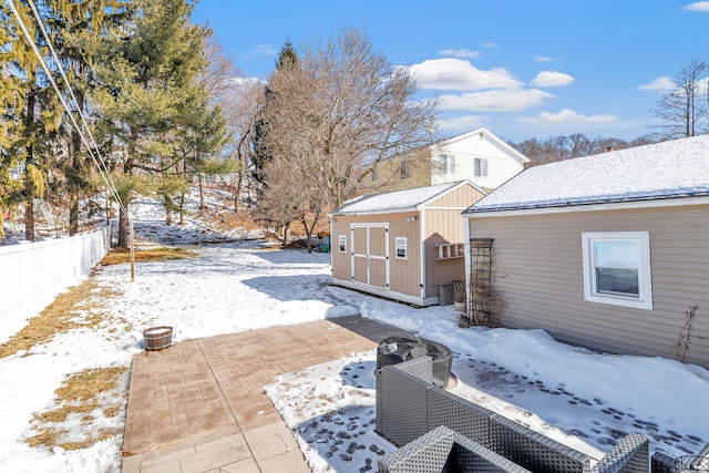 view of snow covered exterior with a patio, an outdoor structure, fence, and a storage unit