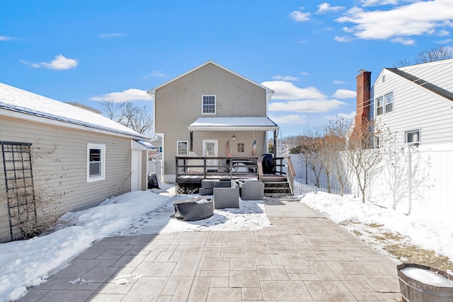 snow covered rear of property featuring a patio area, fence, and a wooden deck