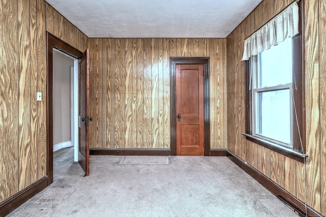 unfurnished room with baseboards, wooden walls, and carpet