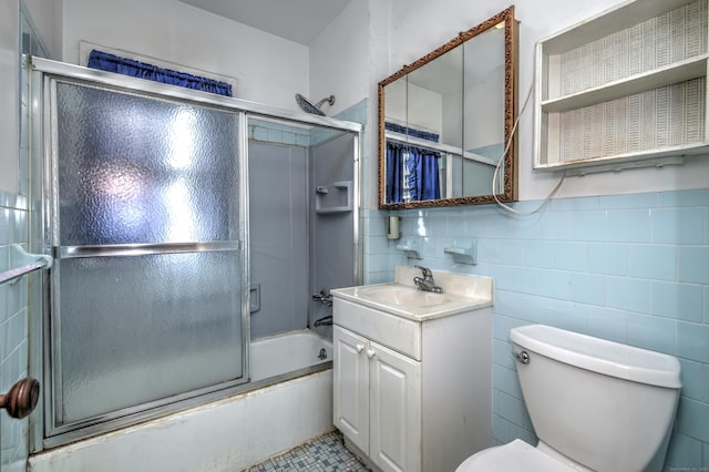 bathroom featuring toilet, vanity, tile walls, and bath / shower combo with glass door