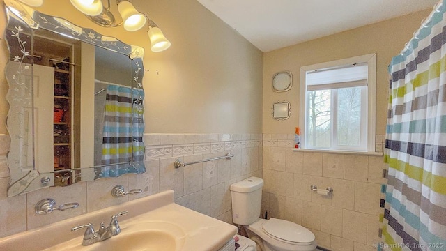 full bathroom featuring toilet, a wainscoted wall, curtained shower, and vanity