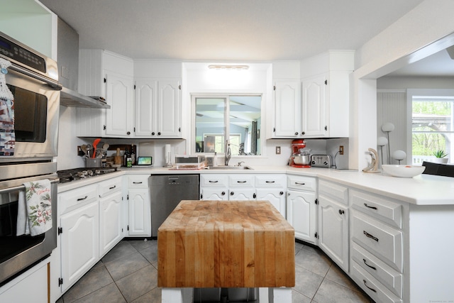 kitchen featuring a peninsula, stainless steel appliances, white cabinets, tile patterned flooring, and light countertops