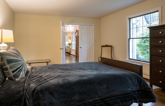 bedroom with multiple windows, an inviting chandelier, wood finished floors, and a baseboard heating unit
