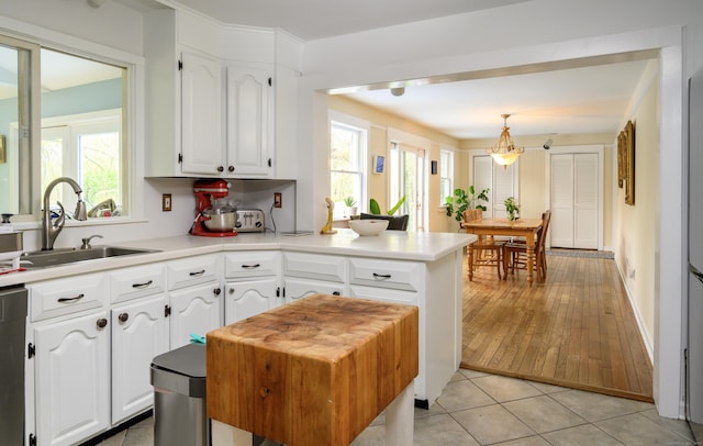 kitchen featuring a sink, a peninsula, pendant lighting, light countertops, and white cabinets