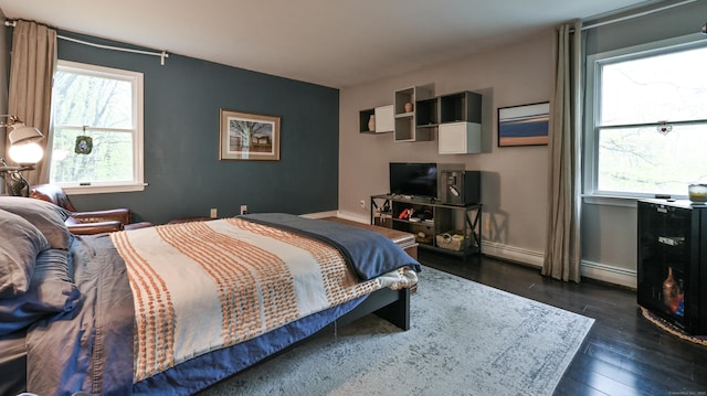 bedroom with multiple windows, dark wood-style flooring, baseboards, and a baseboard heating unit